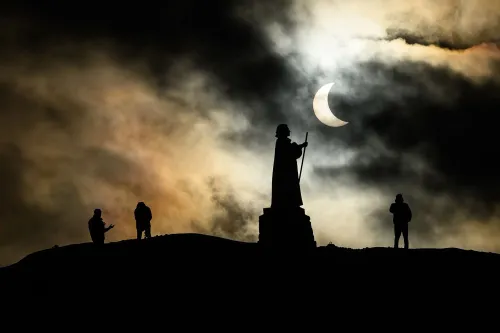 صورة تظهر كسوفًا جزئيًا للشمس خلف سحب داكنة، مع silhouettes لعدة أشخاص يقفون في المقدمة، مما يبرز جمال الحدث السماوي.