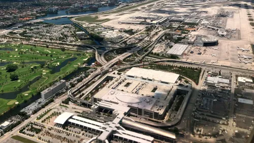 صورة جوية لمطار ميامي تُظهر المرافق والممرات والطرق المحيطة، مع مساحات خضراء وممرات مائية، تعكس حركة الطيران والنقل.