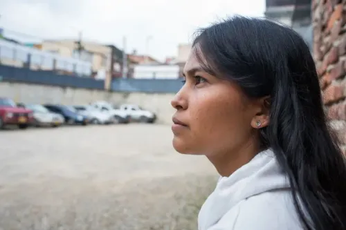 صورة لامرأة شابة ذات شعر طويل، تنظر بتفكير بينما تجلس في ساحة خارجية، مع سيارات خلفها، تعكس تحديات إعادة الاندماج بعد الإفراج عنهم من السجن.