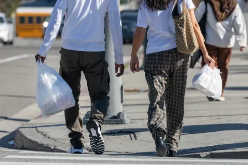 زوجان يسيران في الشارع حاملاً أكياسًا بلاستيكية، مما يعكس نمط الحياة اليومية في ظل التحديات الاقتصادية الحالية.