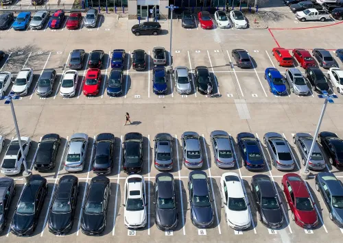صورة تظهر موقف سيارات مزدحم، حيث تتوزع السيارات بألوان وأشكال متنوعة، مما يعكس أزمة قروض السيارات وتأثيرها على الاقتصاد الأمريكي.