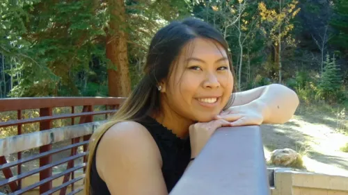 ماغي لونغ، طالبة في مدرسة بلات كانيون الثانوية، تبتسم بمرح وهي تستند على حاجز خشبي وسط الغابات، استعدادًا لحدث موسيقي.