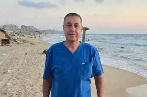 الدكتور حسام أبو صفية، مدير مستشفى كمال عدوان، يقف على شاطئ غزة مرتديًا زيًا طبي، وسط أجواء هادئة تعكس معاناته في السجن.