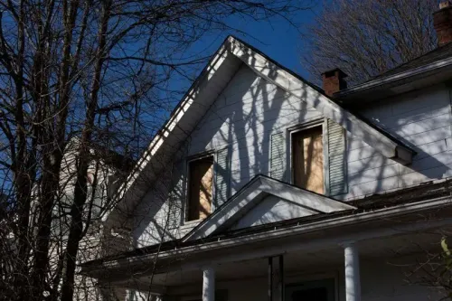 منزل مهجور في واتربري، مع نوافذ مغطاة بألواح خشبية، يتوسطه ظلال الأشجار، يشير إلى مأساة عائلية مؤلمة.