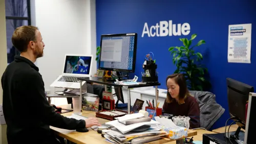 مكتب ActBlue يظهر موظفين يعملون على أجهزة الكمبيوتر، مع التركيز على بيئة العمل الديناميكية التي تدعم جمع التبرعات الديمقراطية.