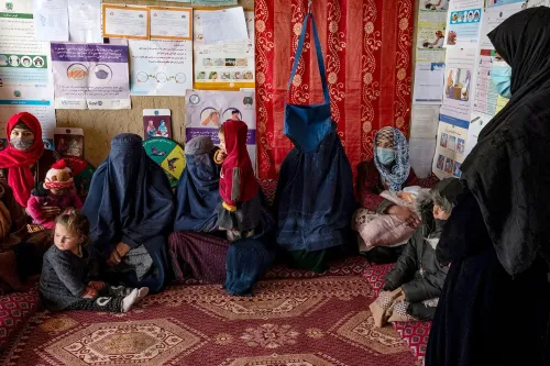نساء وأطفال يجلسون في مركز دعم في أفغانستان، يعكس تأثير سوء التغذية والأزمات الإنسانية، مع وجود ملصقات توعوية على الجدران.