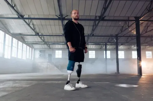 شاب مبتور الساقين يقف في مساحة داخلية، يعكس قوة الإرادة والتصميم بعد تحدياته في سباق الرجل الحديدي.