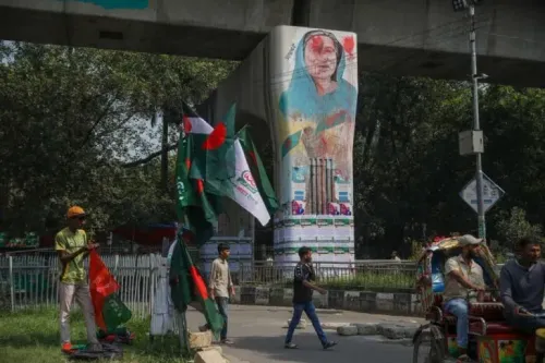 جدارية كبيرة لشيخة حسينة تحت جسر في دكا، مع وجود رجال يحملون أعلام بنغلاديش، تعكس الأجواء السياسية المتوترة في البلاد.