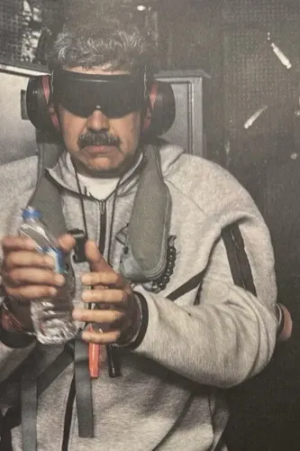 رجل يرتدي نظارات واقية وسماعات، ممسكًا بزجاجة ماء، يبدو عليه التوتر في ظل الأوضاع السياسية المتوترة في فنزويلا.