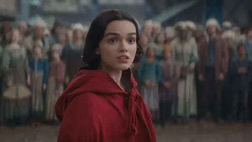 تظهر الصورة الأميرة "بياض الثلج" مرتدية رداء أحمر، وسط حشد من الناس في مشهد من فيلم الحركة الحية.