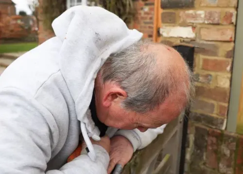 رجل مسن ينحني فوق قفص أثناء محاولة الإمساك بصقر هاريس الذي هاجم سكان قريته، مما أدى إلى إصابات واضطرابات في الحياة اليومية.