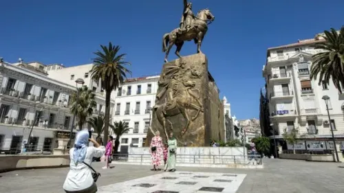 تمثال يُظهر الفارس على حصانه في ساحة الجزائر، حيث تتجمع النساء لالتقاط الصور، محاطًا بأشجار النخيل والمباني التاريخية.