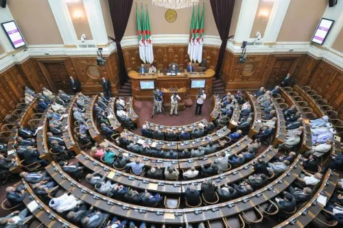 جلسة مجلس الشعب الوطني الجزائري مكتظة بالأعضاء وسط أعلام الجزائر، تعكس الاستعدادات للانتخابات التشريعية في يوليو 2023.