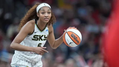 لاعبة كرة السلة أنجيل ريس من فريق شيكاغو سكاي تحمل الكرة وتستعد للتمرير خلال مباراة، مع أجواء حماسية في الملعب.