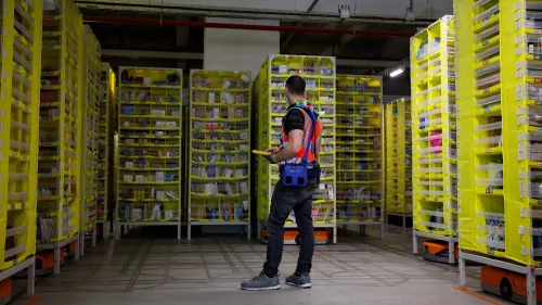 موظف في مستودع أمازون يتفقد رفوف التخزين المليئة بالسلع، مما يعكس تأثير الذكاء الاصطناعي على القوى العاملة.