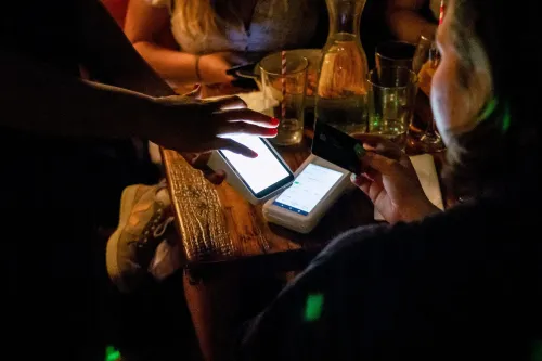 شخص يستخدم هاتفه الذكي للدفع في مطعم، بينما تحمل شخص آخر بطاقة ائتمان، مما يعكس سلوك المستهلكين في ظل التوترات الاقتصادية.