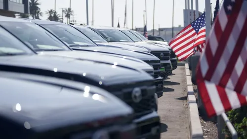صف من السيارات السوداء في معرض سيارات أمريكي، مع أعلام الولايات المتحدة تتمايل في الخلفية، تعكس زيادة في قروض السيارات والديون.