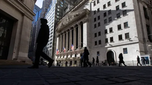 مشهد لشارع مزدحم بالقرب من بورصة نيويورك، حيث يسير الناس تحت ظلال المباني الشاهقة، مما يعكس القلق الاقتصادي السائد.