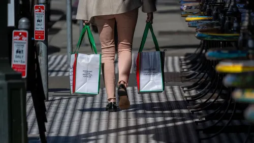 امرأة تحمل أكياس تسوق بينما تسير في الشارع، مما يعكس زيادة الإنفاق الاستهلاكي في ظل التغيرات الاقتصادية والسياسات التجارية.