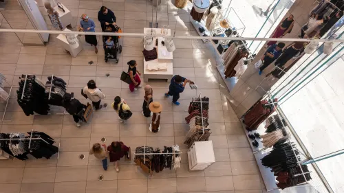 متسوقون يتجولون في متجر ملابس عصري، معروضات متنوعة من الملابس، مما يعكس تراجع إنفاق المستهلكين في أبريل.