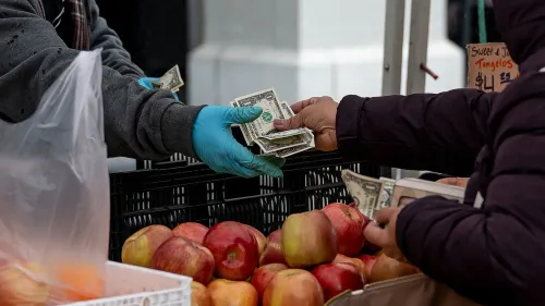 تبادل الأموال في سوق محلي، حيث يشتري شخص تفاحًا طازجًا، مما يعكس زيادة إنفاق المستهلكين في فبراير.