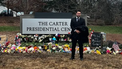 رجل يقف أمام مركز كارتر الرئاسي، محاطًا بالزهور والرسائل التذكارية، تعبيرًا عن الحب والاحترام للرئيس الأسبق جيمي كارتر.