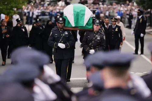 موكب جنازة ضابط شرطة يحمل النعش المغطى بعلم، مع حضور كبير من رجال الشرطة والمواطنين في الشارع، يعكس أجواء الحزن والتضامن.