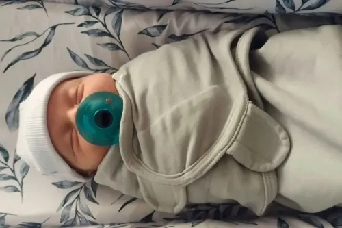 طفل رضيع حديث الولادة ملفوف في بطانية، يحمل مصاصة، مع خلفية من أقمشة مزخرفة، يمثل قصة ولادة فريدة من جنين مجمد لأكثر من 30 عامًا.