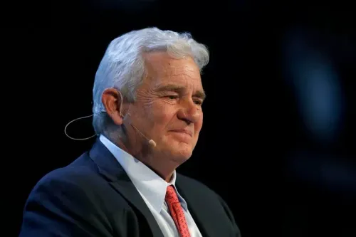 صورة لرجل مسن ذو شعر أبيض، مبتسم، يرتدي بدلة رسمية، يتحدث في مؤتمر. تعكس تعابيره الثقة والقيادة في سياق قضية قانونية معقدة.