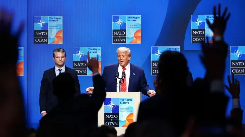 ترامب يتحدث في مؤتمر صحفي خلال قمة الناتو، مع وجود صحفيين يرفعون أيديهم لطرح الأسئلة، خلفية تحمل شعارات الناتو.