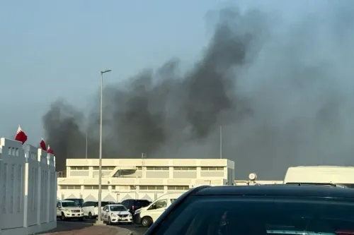 تصاعد دخان أسود من موقع الهجوم الإسرائيلي في قطر، مع وجود سيارات متوقفة وأعلام قطرية في الخلفية، مما يعكس تصاعد التوترات الإقليمية.