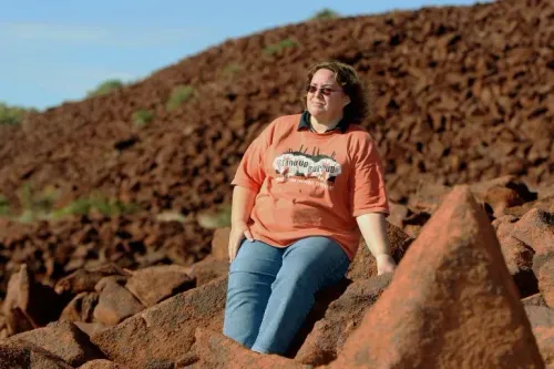 امرأة جالسة على صخور حمراء في موقع موروجوغا الأثري، تعبر عن سعادتها بإدراج الموقع في قائمة التراث العالمي لليونسكو.