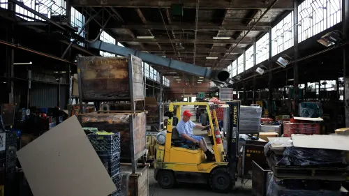 عامل يقود رافعة شوكية صفراء داخل مستودع مزدحم بالصناديق والمواد، مما يعكس نشاط السوق وتأثيرات التضخم على الأسعار.