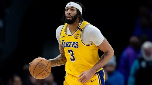 أنتوني ديفيس، لاعب كرة السلة، يرتدي زي لوس أنجلوس ليكرز، يحمل الكرة ويستعد للعب، مع تعبير عن التركيز والعزيمة.