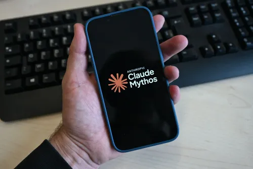 شخص يحمل هاتفًا ذكيًا يظهر عليه شعار "Claude Mythos" الخاص بشركة Anthropic، مع لوحة مفاتيح في الخلفية، في سياق قرار حكومي يؤثر على نماذج الذكاء الاصطناعي.