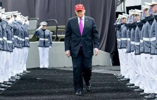 ترامب يسير بين صفوف من العسكريين في الأكاديمية العسكرية، مرتديًا قبعة تشير إلى حملته الانتخابية، مع خلفية عسكرية.