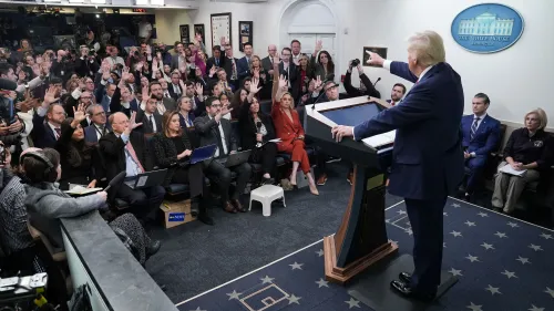 ترامب يتحدث في مؤتمر صحفي بالبيت الأبيض بينما يرفع الصحفيون أيديهم لطرح الأسئلة، مما يبرز التوتر حول حرية الصحافة.