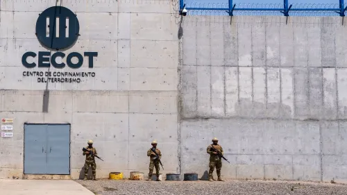 جدار مركز احتجاز "CECOT" في السلفادور، مع جنود مسلحين يقفون أمام المدخل، مما يعكس التوترات المتعلقة بعمليات الترحيل.