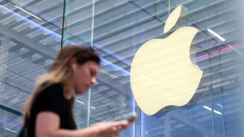 امرأة تحمل هاتفًا ذكيًا تسير بجانب شعار شركة آبل في متجر، مما يعكس اهتمام آبل بتطوير متصفح سفاري مع التركيز على الذكاء الاصطناعي.