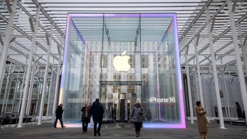 واجهة متجر آبل الزجاجية تعرض شعار الشركة وعبارة "آيفون 16"، مع زوار يتجولون حولها، تعكس الابتكار في عالم التكنولوجيا.