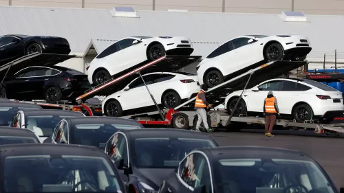 شاحنات تنقل سيارات تسلا الجديدة، مع سيارات بيضاء وسوداء متراكمة، تعكس تراجع مبيعات تسلا وزيادة المنافسة في السوق.