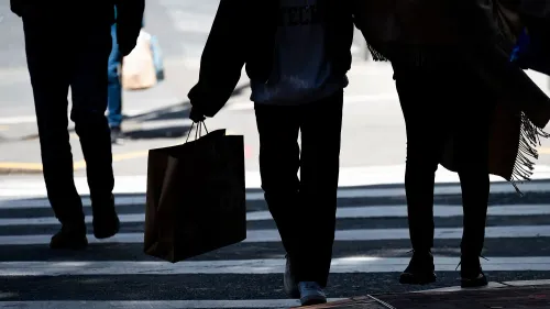 أشخاص يعبرون الشارع حاملي حقائب التسوق، مما يعكس تراجع إنفاق المستهلك في الاقتصاد الأمريكي خلال الربع الأول.