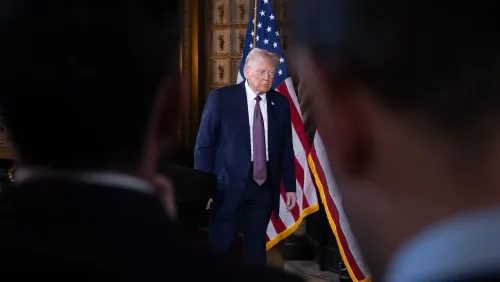 دونالد ترامب يسير نحو الواجهة، خلفه أعلام أمريكية، أثناء فترة انتقالية لرئاسته. يُظهر الصورة سياق المناقشات السياسية والمفاوضات.