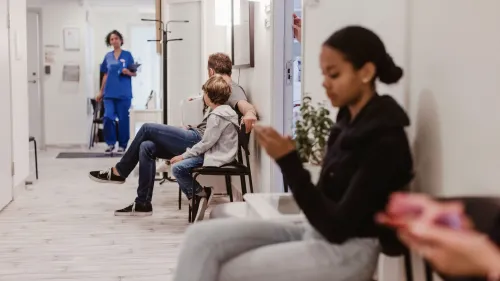 انتظارات المرضى في عيادة طبية، حيث يجلس مجموعة من الأفراد في قاعة الانتظار، بينما يخرج ممارس صحي.