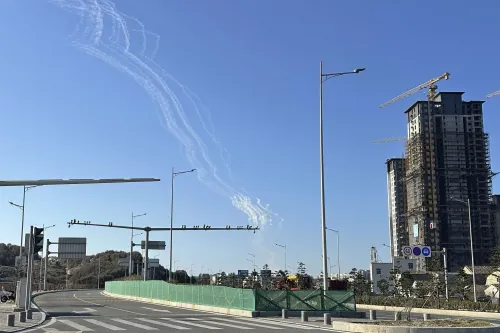 خطوط بيضاء من دخان الطائرات تتصاعد في السماء الزرقاء فوق مدينة قيد الإنشاء، مما يعكس التوترات العسكرية المتزايدة في المنطقة.