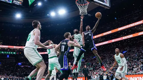 لاعب من فريق ساكرامنتو كينجز يسجل نقطة خلال مباراة مثيرة ضد بوسطن سلتكس، مع وجود لاعبين من الفريقين في الملعب.