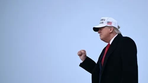 ترامب يسير مرتديًا قبعة تحمل شعار "اجعل أمريكا عظيمة مرة أخرى"، مع تعبير جاد، في خلفية رمادية.