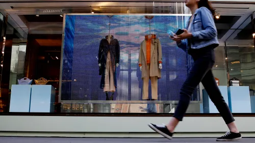 واجهة متجر تعرض ملابس فاخرة، مع عارضتين في الخلفية، بينما يمر أحد المتسوقين في المقدمة. تعكس الصورة تحول العلامات التجارية لجذب المستهلكين الطموحين.
