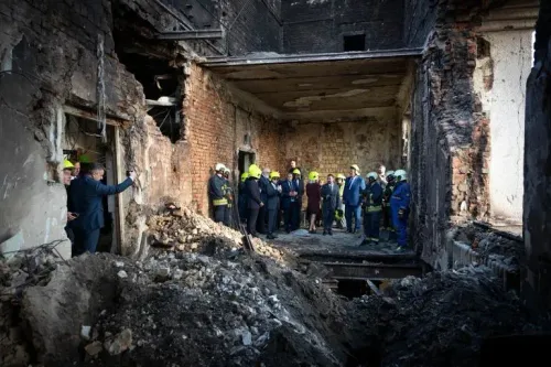 مجموعة من الأشخاص يرتدون خوذات واقية يتجمعون في موقع دمار، حيث تظهر الجدران المتضررة والأرض المليئة بالركام بعد الهجوم.