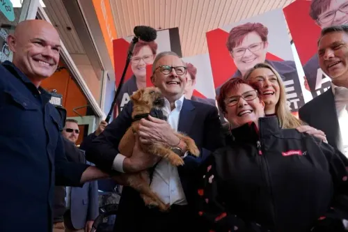 رئيس الوزراء الأسترالي أنتوني ألبانيز مبتسمًا وهو يحمل كلبًا، محاطًا بداعميه في حملة انتخابية، مع لافتات انتخابية خلفهم.